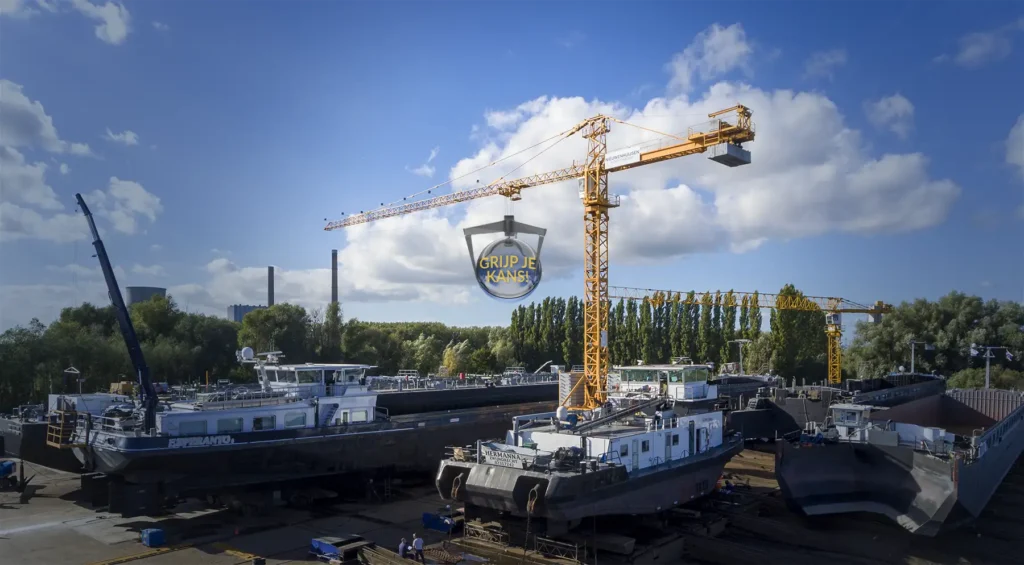 Grote kraan heeft met zijn grijper een bal vast waarop een winkans geschreven staat. Het beeld hoort bij een winactie op een beurs.